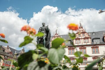 Eine Statue vor einem Haus mit Fachwerkelementen, davor Blumen