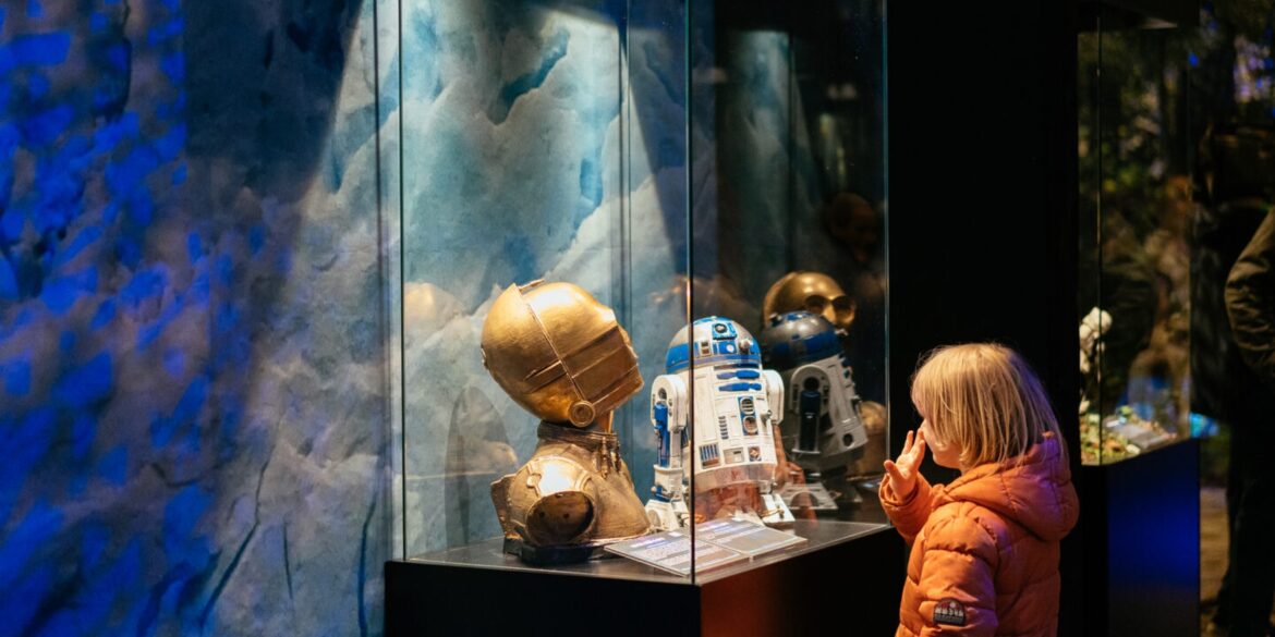 Ein Kind steht in einer Ausstellung vor einer Vitrine mit dem Kopf von C3PO