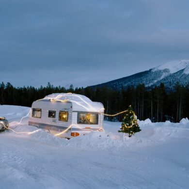 Ein überschneiter Wohnwagen ist mit einer Lichterkette umwickelt, daneben steht ein Weihnachtsbaum