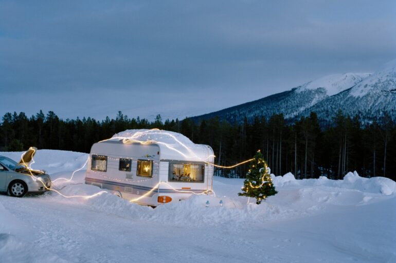 Ein überschneiter Wohnwagen ist mit einer Lichterkette umwickelt, daneben steht ein Weihnachtsbaum