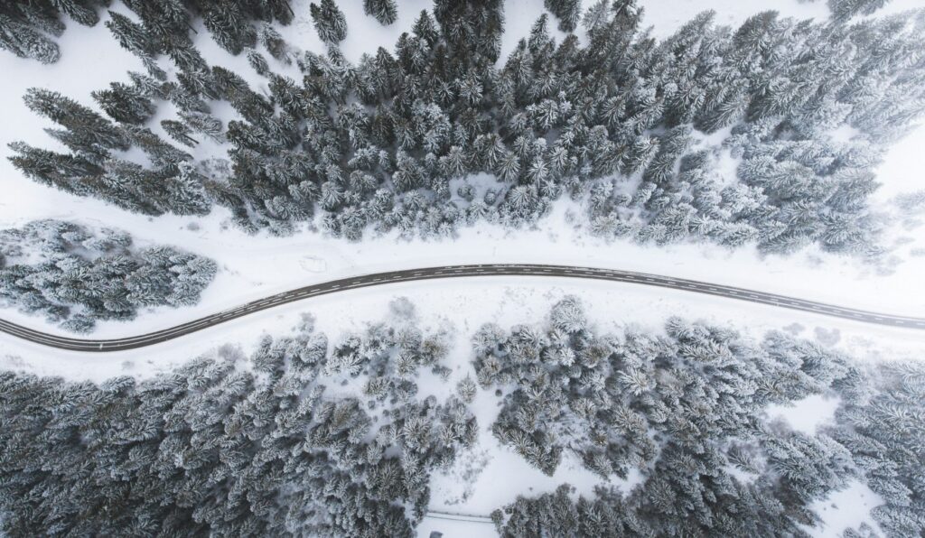 From a bird's eye view, a road winds through a snow-covered coniferous forest.