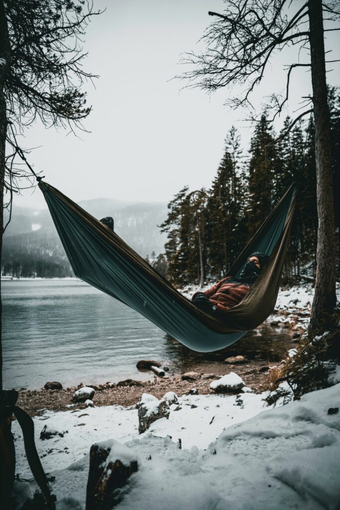 A person is lying in a hammock by a wintery lake.