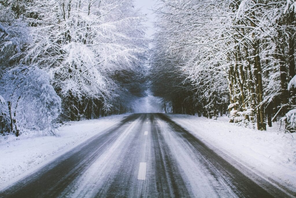 Eine verschneite Straße führt in einen Wald hinein