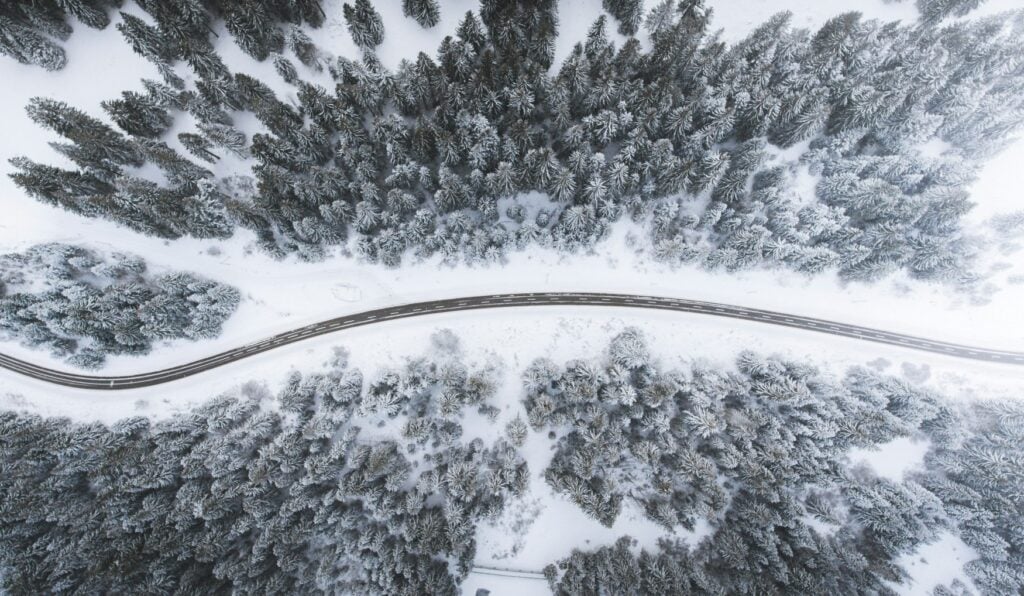 Aus der Vogelperspektive schlängelt sich eine Straße durch einen verschneiten Nadelwald