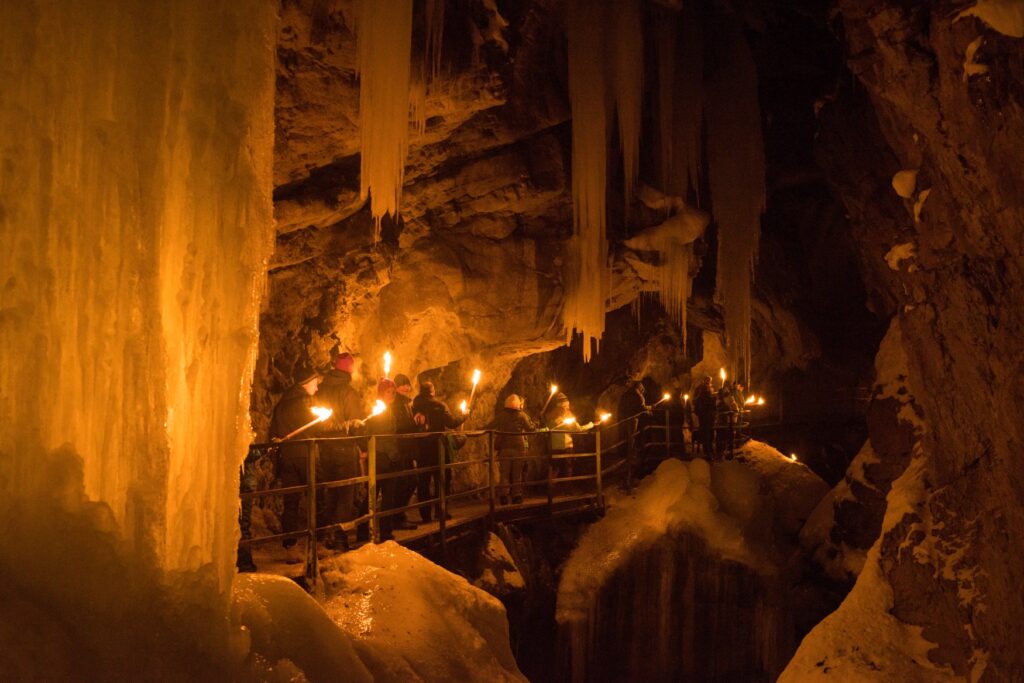 Eine Gruppe Menschen zieht mit Fackeln über einen befestigten Weg in einer Tropfsteinhöhle