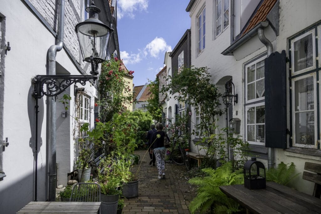 Eine schmale Straße im Lübecker Gängeviertel, weiße Fassaden strahlen im Sonnenlicht