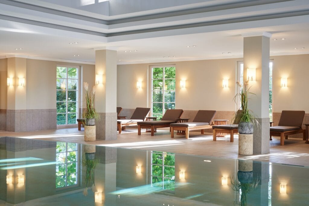 Ein großer Indoor-Pool im Strandhotel Zingst. Am Rand des Raums stehen einige Ruheliegen aus Holz