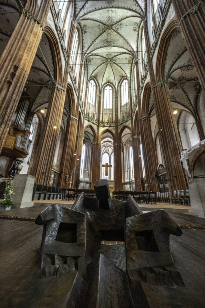 Skulptur eines Menschen mit offenen Armen in St. Marien in Lübeck, im Hintergrund erhebt sich der Chor