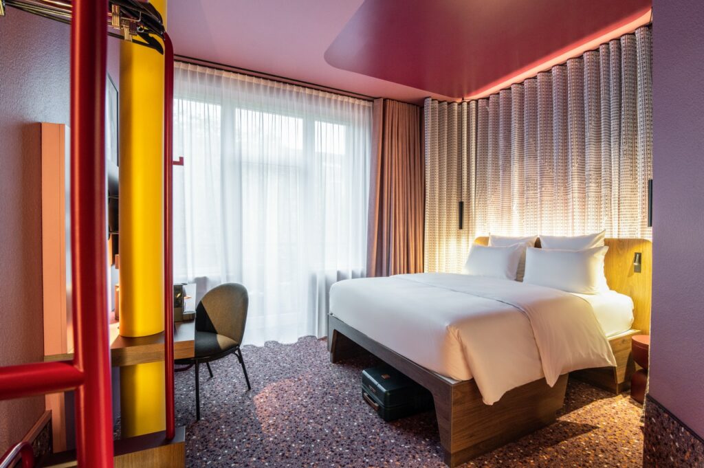 A room in the newly opened Tribe hotel in Düsseldorf, with carpeted floors, elegant lighting and a pink ceiling.