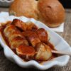 A curry sausage in a ceramic bowl, with a bread roll in the background