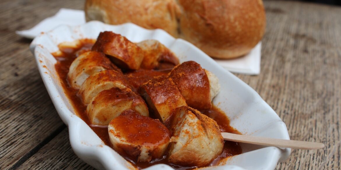 A curry sausage in a ceramic bowl, with a bread roll in the background