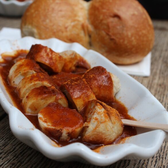 A curry sausage in a ceramic bowl, with a bread roll in the background