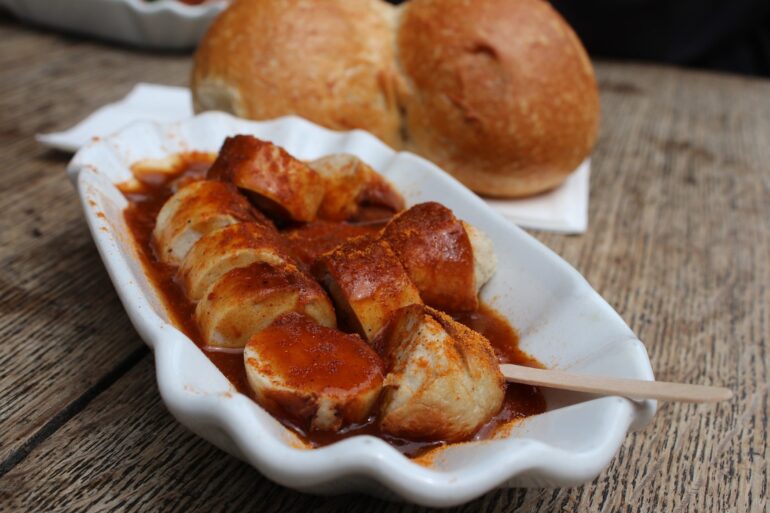 A curry sausage in a ceramic bowl, with a bread roll in the background