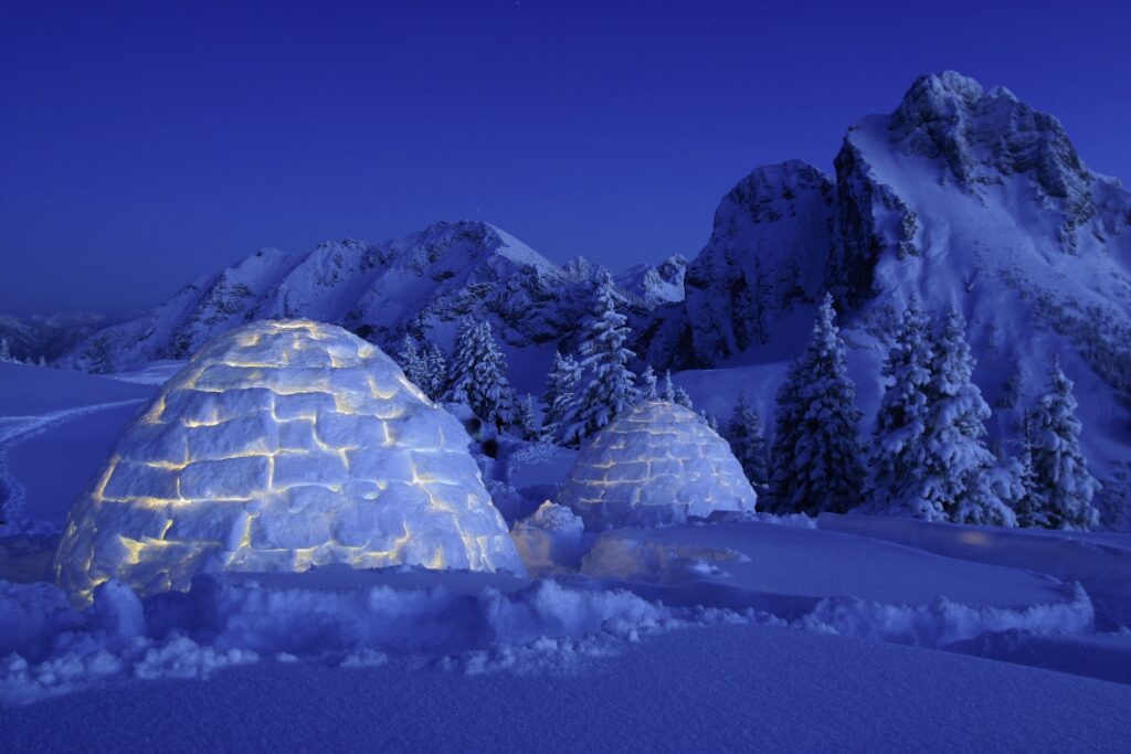 An igloo in the snow-covered town of Pfronten in the Allgäu region at night. It is illuminated from within.