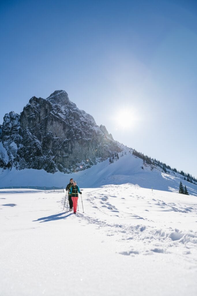 Zwei Menschen wandern auf Schneeschuhen durchs verschneite Allgäu, im Hintergrund eine Bergspitze