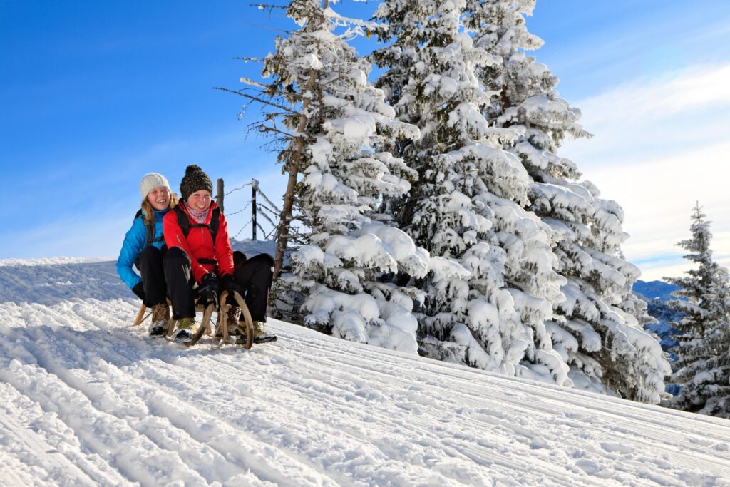 Two people are riding down a snowy slope near Pfronten in Allgäu on a wooden sled.