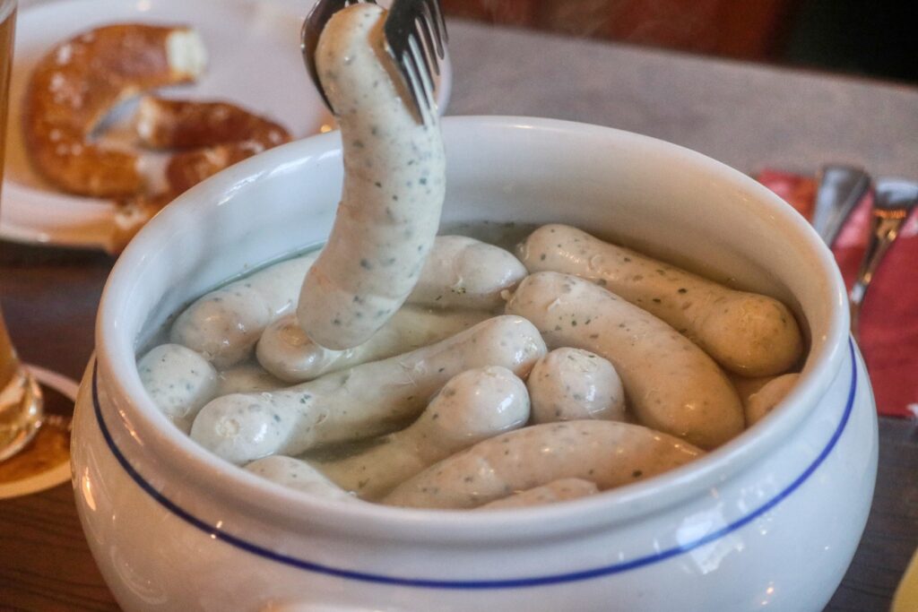 A bowl of white sausages, with a pretzel on the table in the background