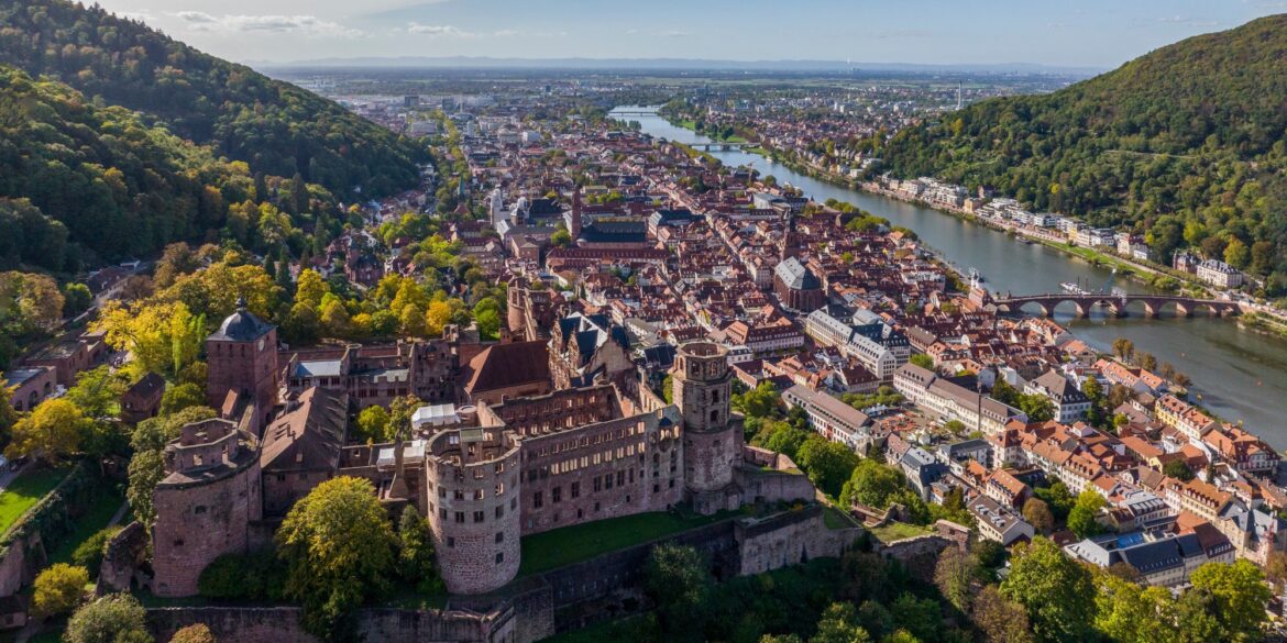 Drohnenansicht der Stadt Heidelberg, links im Vordergrund das Schloss, darunter im Tal die Altstadt und dann der Neckar. Aufgenommen an einem sonnigen Sommertag.