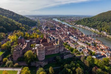 Drohnenansicht der Stadt Heidelberg, links im Vordergrund das Schloss, darunter im Tal die Altstadt und dann der Neckar. Aufgenommen an einem sonnigen Sommertag.