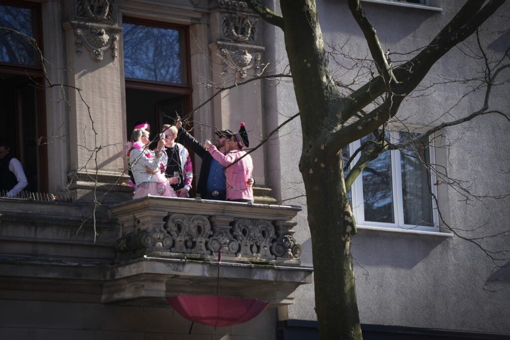 Vier Personen in rosa Kostümen stehen auf einem Balkon und machen ein Selfie.