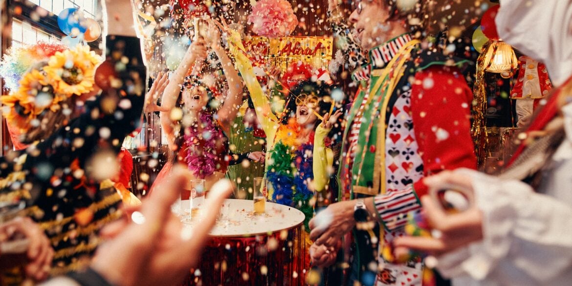 Menschen in Kostümen feiern in einer Kneipe Karneval, der Großteil des Bildes ist von Konfetti ausgefüllt.