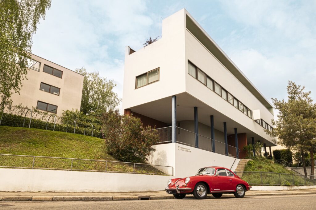 The Weissenhof Museum in Stuttgart, an angular white building. In the foreground, a red vintage Porsche