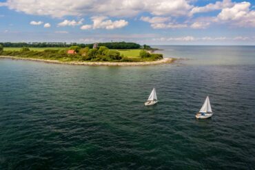 Zwei Segelboote fahren auf der Ostsee, im Hintergrund die Insel Fehrmarn. Ein beliebtes Ausflugsziel von Kiel aus