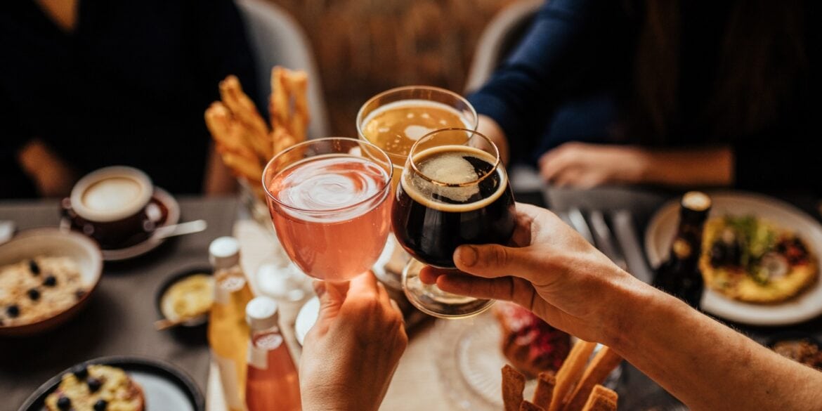 Three people toast with different drinks over a set table