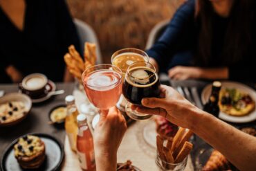 Three people toast with different drinks over a set table