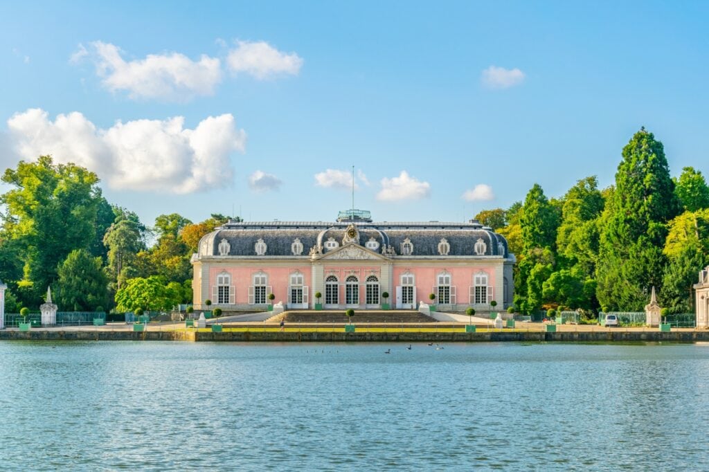 Schloss Benrath mit seiner rosa Fassade im Sonnenlicht, davor der Teich