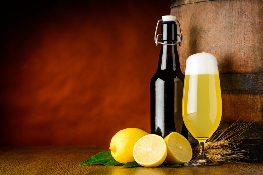 A flip-top bottle next to a beer tulip with a shandy, next to it are some lemons.