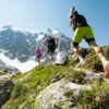 Eine Gruppe Menschen läuft einen Hang hinauf, im Hintergrund schneebedeckte Berge