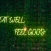 Ein Neon-Schriftzug "Eat Well, Feel Good" vor dunklem Hintergrund