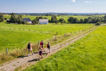 Eine vierköpfige Familie wandert im Sonnenschein über einen Feldweg im Bergischen Land