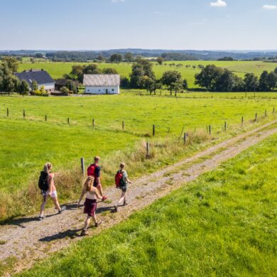 Eine vierköpfige Familie wandert im Sonnenschein über einen Feldweg im Bergischen Land