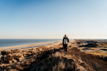 Eine Frau in Wanderkleidung steht auf einer Düne an der Nordsee