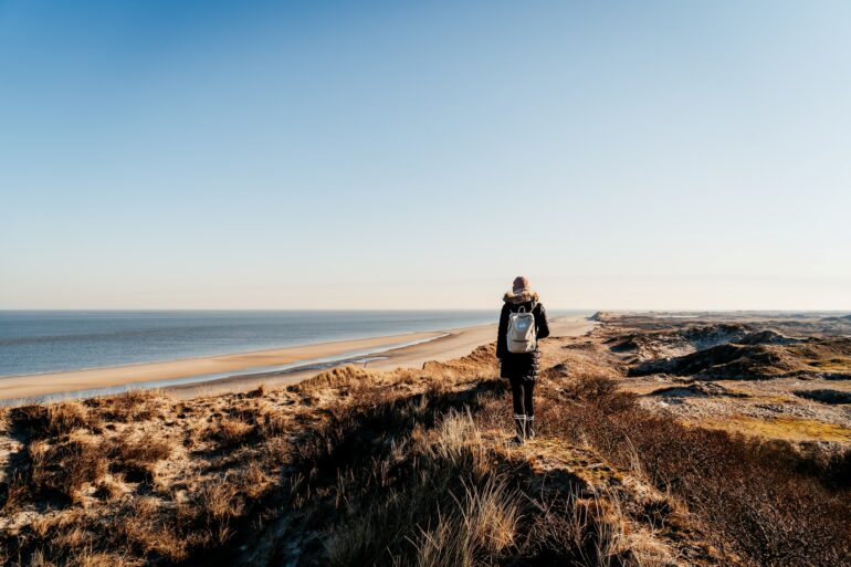 Eine Frau in Wanderkleidung steht auf einer Düne an der Nordsee