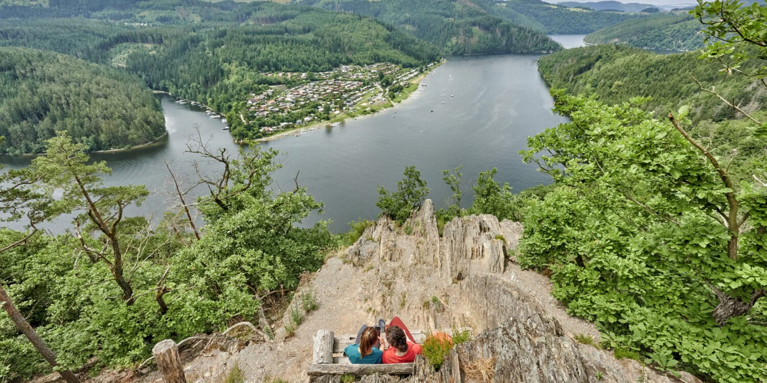 Zwei Personen sitzen auf einer Bank auf einer Anhöhe über dem Hohenwartestausee im Thüringer Meer
