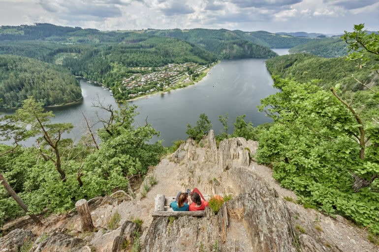 Zwei Personen sitzen auf einer Bank auf einer Anhöhe über dem Hohenwartestausee im Thüringer Meer