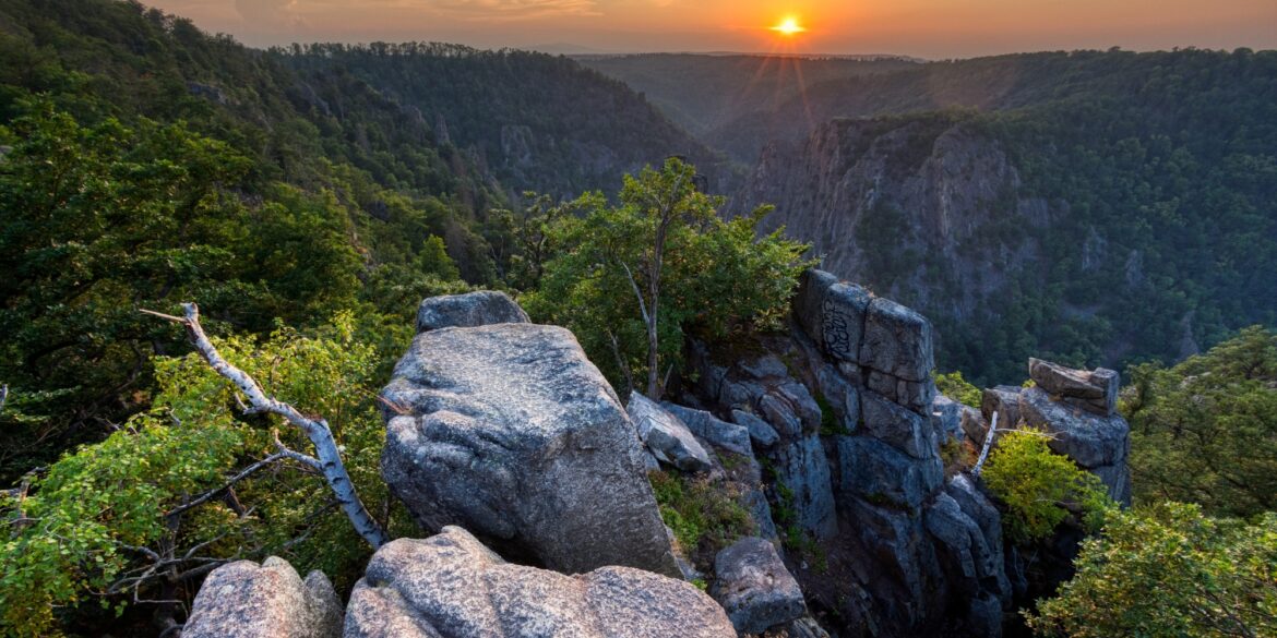 Blick von einer Erhebung in ein Felsental im Nationalpark Harz in Deutschland, über dem die Sonne untergeht.