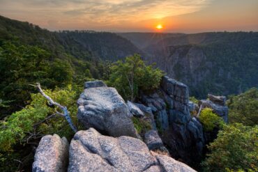 Blick von einer Erhebung in ein Felsental im Nationalpark Harz in Deutschland, über dem die Sonne untergeht.