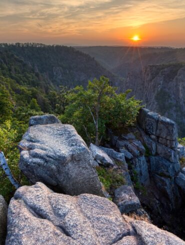 Blick von einer Erhebung in ein Felsental im Nationalpark Harz in Deutschland, über dem die Sonne untergeht.