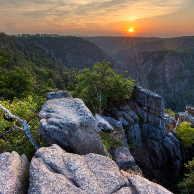 Blick von einer Erhebung in ein Felsental im Nationalpark Harz in Deutschland, über dem die Sonne untergeht.
