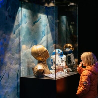 A child stands in front of a display case containing the head of C3PO at an exhibition.