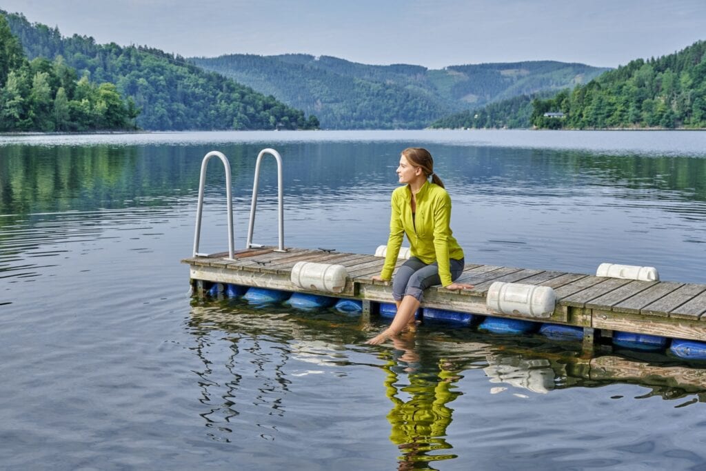 Eine Frau sitzt mit den Beinen im Wasser auf einem Steg am Stausee Hohenwarte im Thüringer Meer