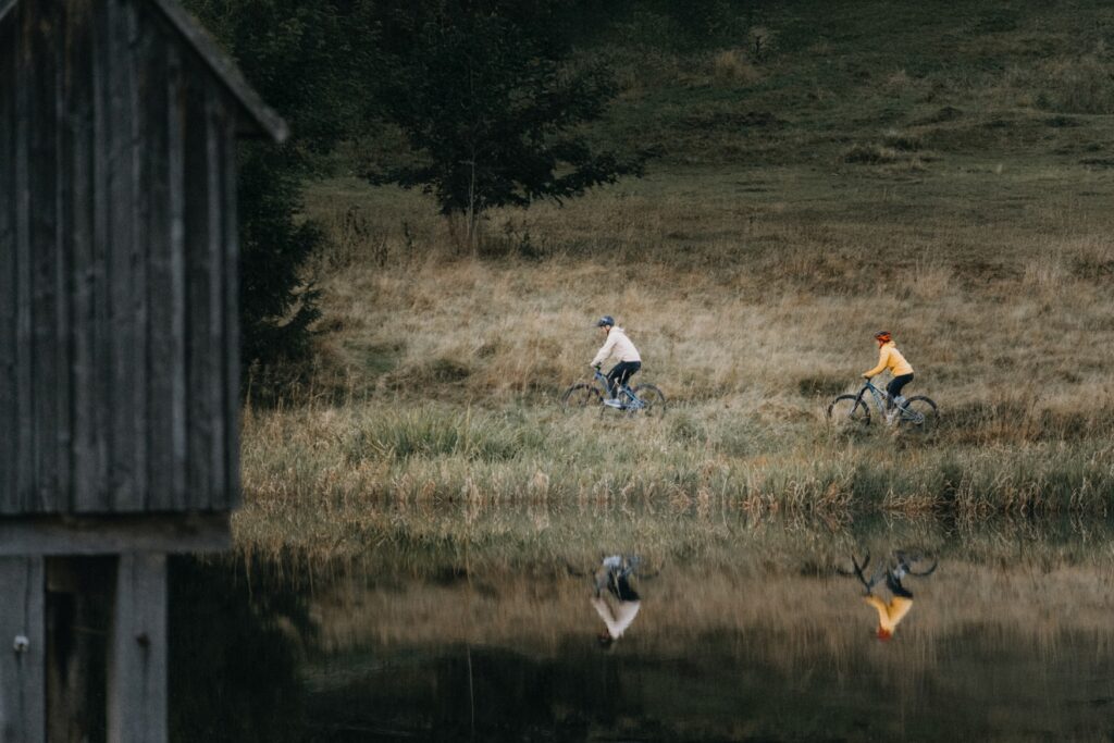 Two people are riding bicycles along a lake.