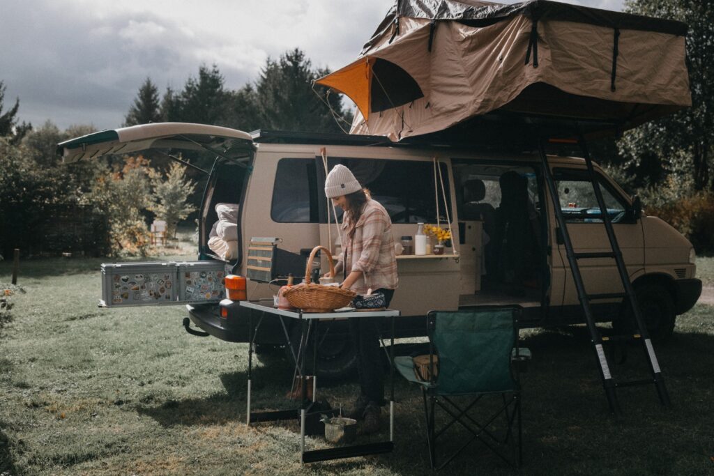 A woman prepares food on a table in front of a camper van.