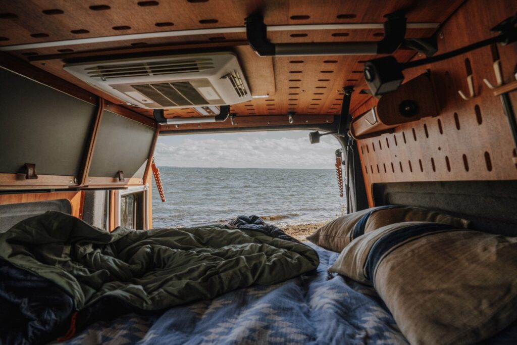 The interior of a camper van at Wildwood Campsite on Rügen, with bed and storage space. The sea can be seen from the open rear.