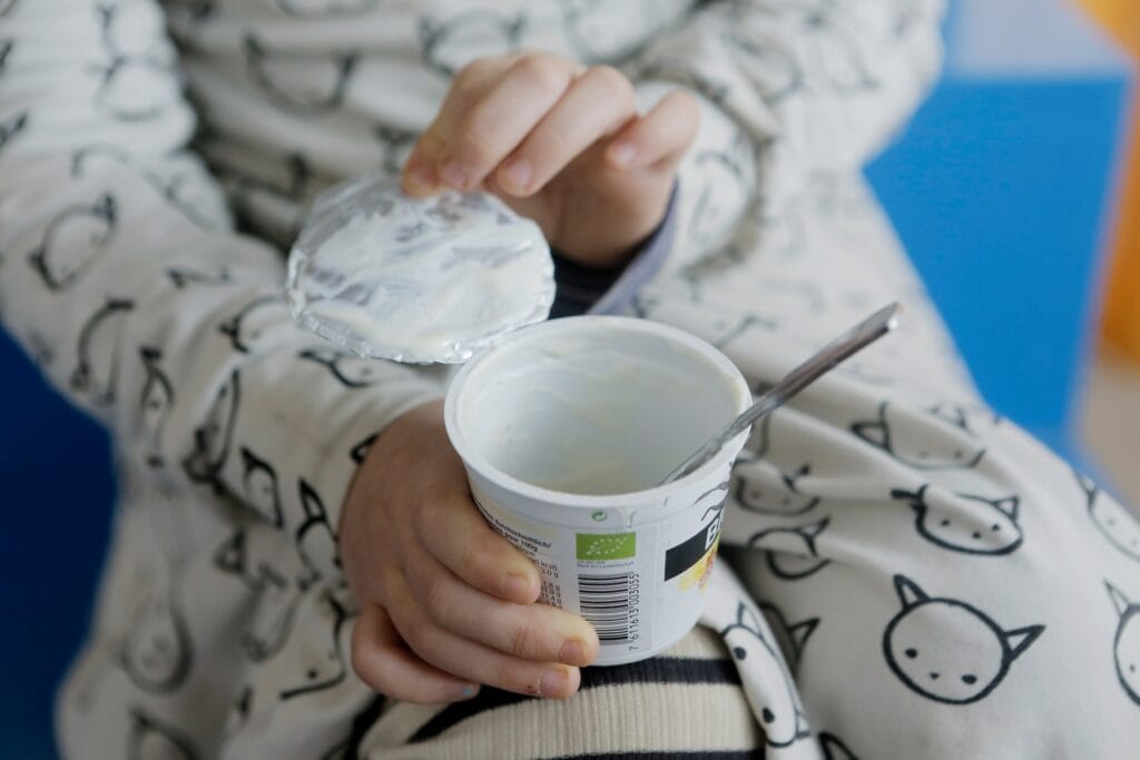 A child holding a yogurt cup, peeling the lid off