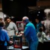 Mehrere Personen stehen in einem nächtlichen Museum um angestrahlte Technik-Exponate herum